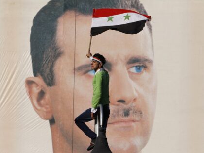 FILE - A pro-Syrian regime protester waves a Syrian flag as he stands in front of portrait