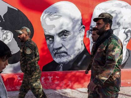 Members of the Popular Mobilization Forces walk past a graffitti depicting General Qassem