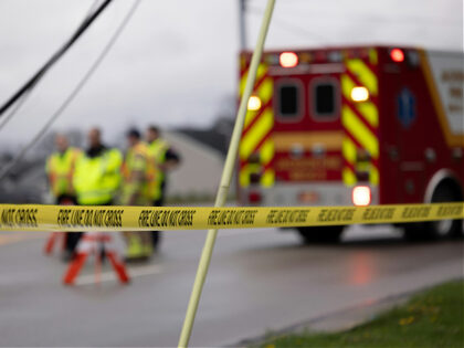 Emergency personnel behind “FIRE LINE DO NOT CROSS” tape near an ambulance.