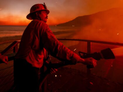 Firefighters work from a deck as the Palisades Fire burns a beachfront property Wednesday,