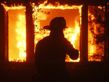 A firefighter is silhouetted in front of a burning structure as the Palisades Fire sweeps