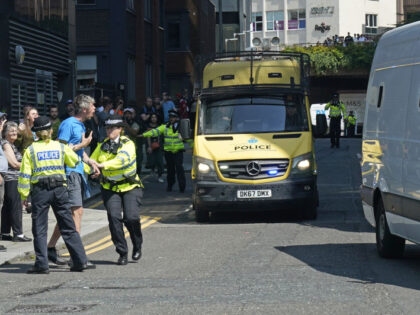 A man is held back by police as a prison van escorted by multiple police vehicles leaves L