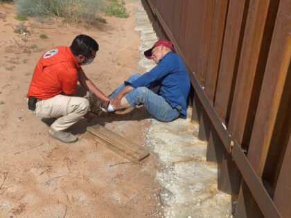 A Mexican official helps a migrant that hurt his leg near the border fence. (Credit INM)