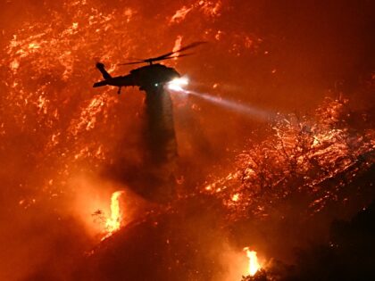 A fire fighting helicopter drops water as the Palisades fire grows near the Mandeville Can