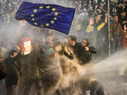 TOPSHOT - Protesters brandishing a European Union flag brace as they are sprayed by a wate