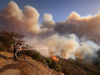 A resident attempts to protect his property from the flames closing in on homes threatened